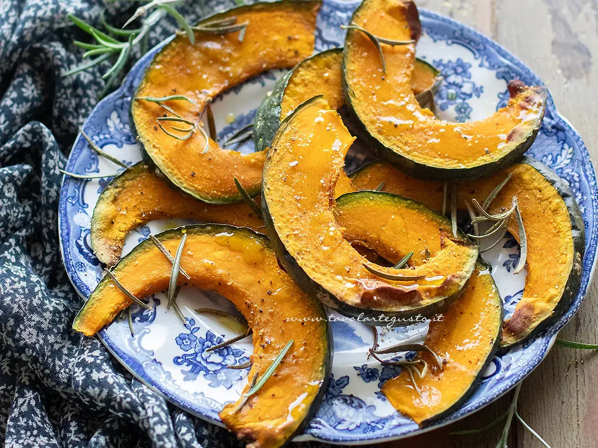Fette di zucca in friggitrice ad aria, dorate e profumate al rosmarino, servite su un piatto blu e bianco.