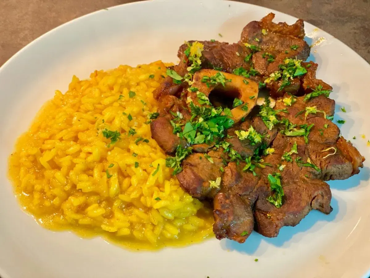 Un piatto di ossobuco alla milanese con risotto giallo, guarnito con prezzemolo fresco e scorza di limone.