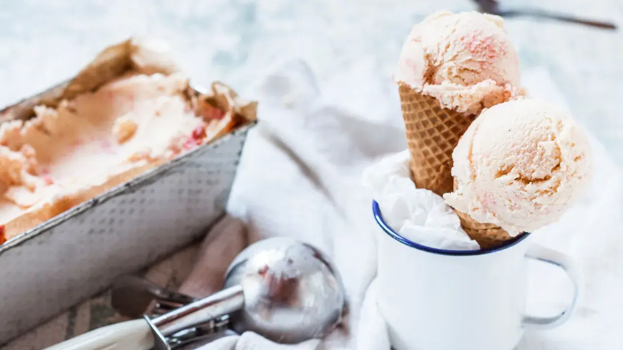 Due palline di gelato fatto in casa, con pezzetti di frutta, in un cono, accanto a una vaschetta e un porzionatore.