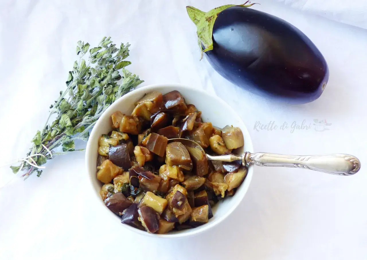 Melanzane in padella, un contorno saporito, con un mazzetto di erbe aromatiche e una melanzana intera.