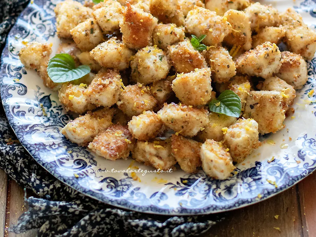 Bocconcini di pollo dorati e croccanti, guarniti con scorza di limone e foglioline di menta, su un piatto decorato.