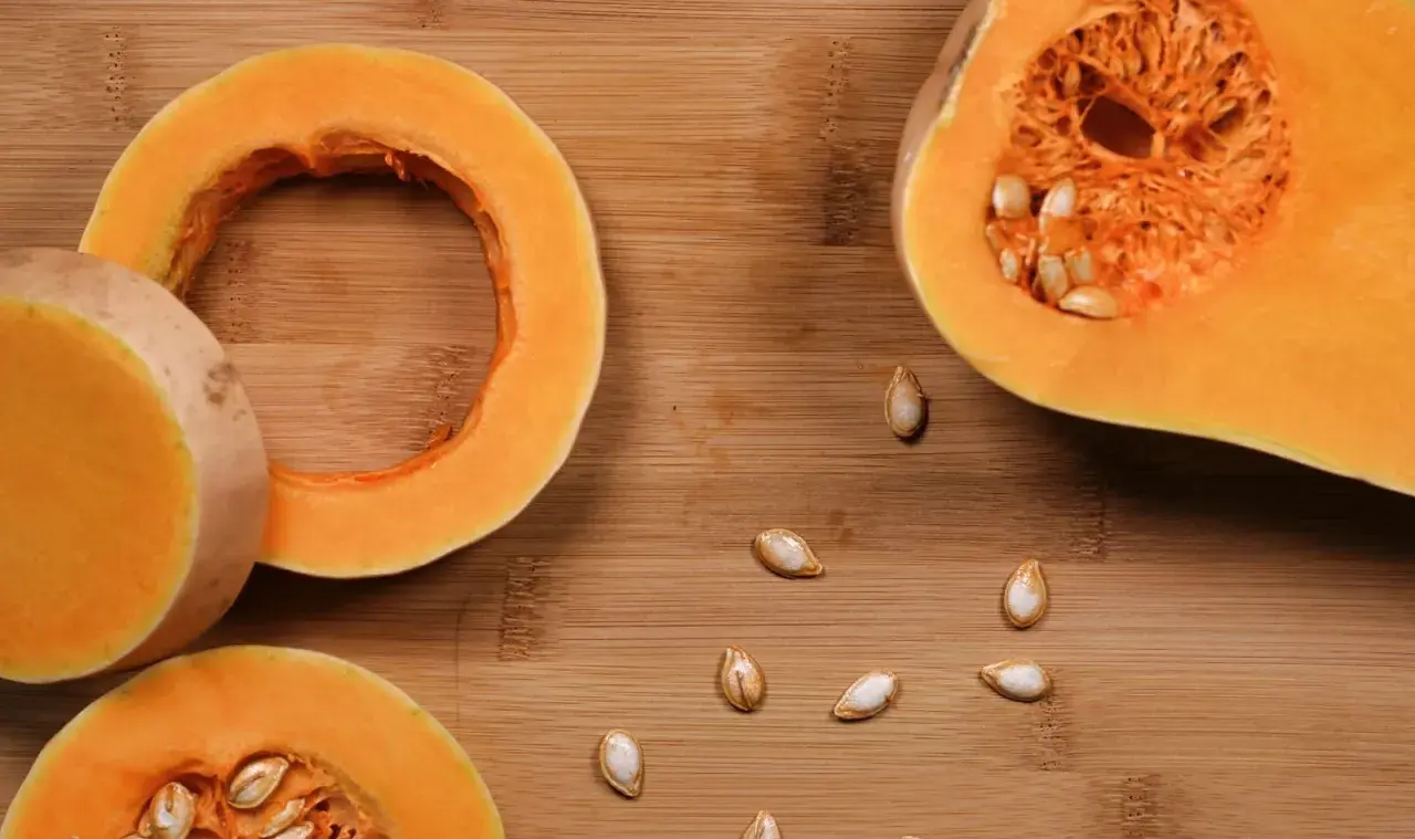 Fette di zucca pronte per essere cotte in padella, con semi sparsi sul tagliere di legno.