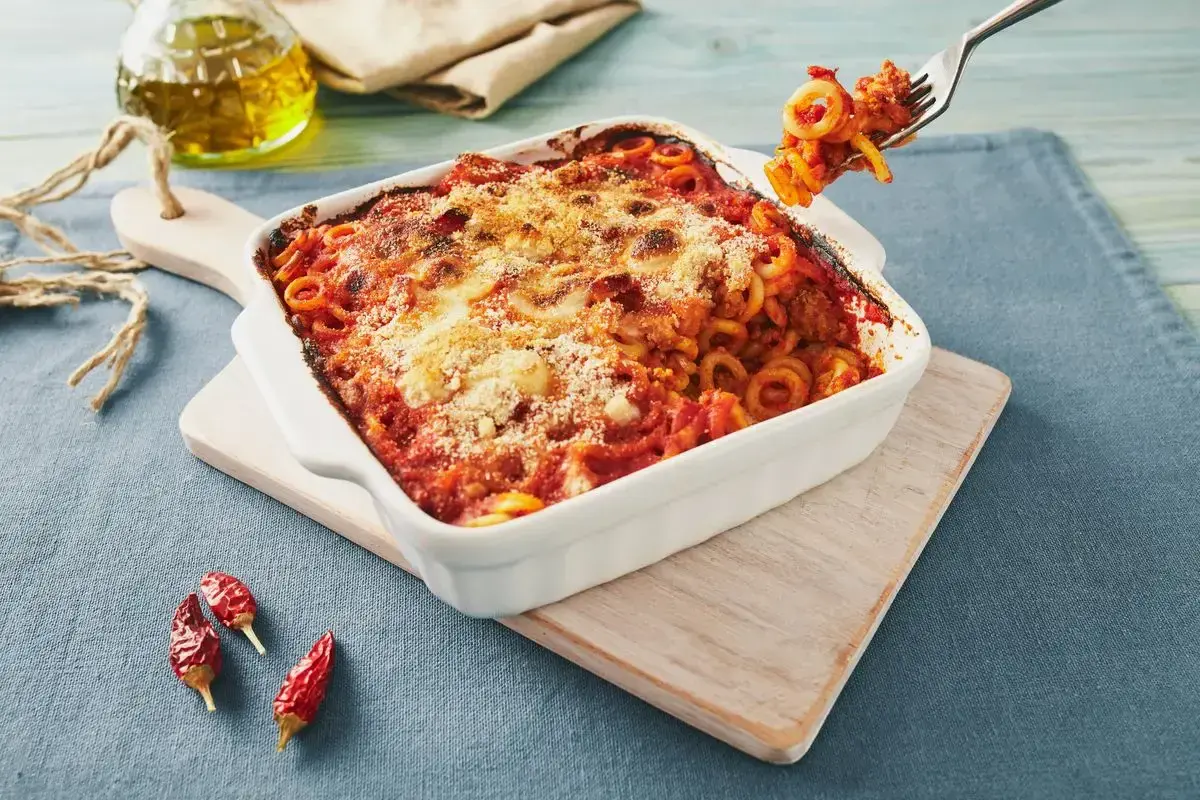 Piatto fumante di pasta alla siciliana, con sugo rosso e formaggio gratinato. Una forchettata pronta per essere gustata.