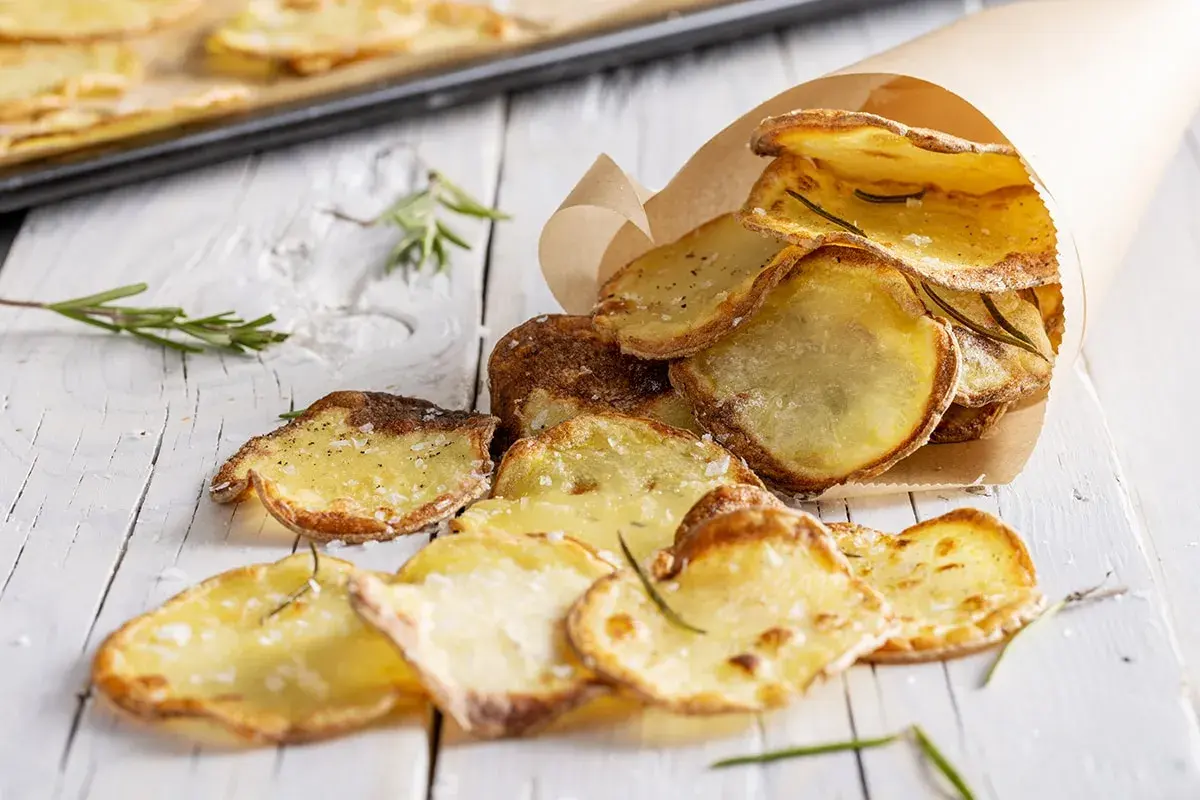 Croccanti chips di patate fatte in casa, condite con sale e rosmarino, servite in un cono di carta.