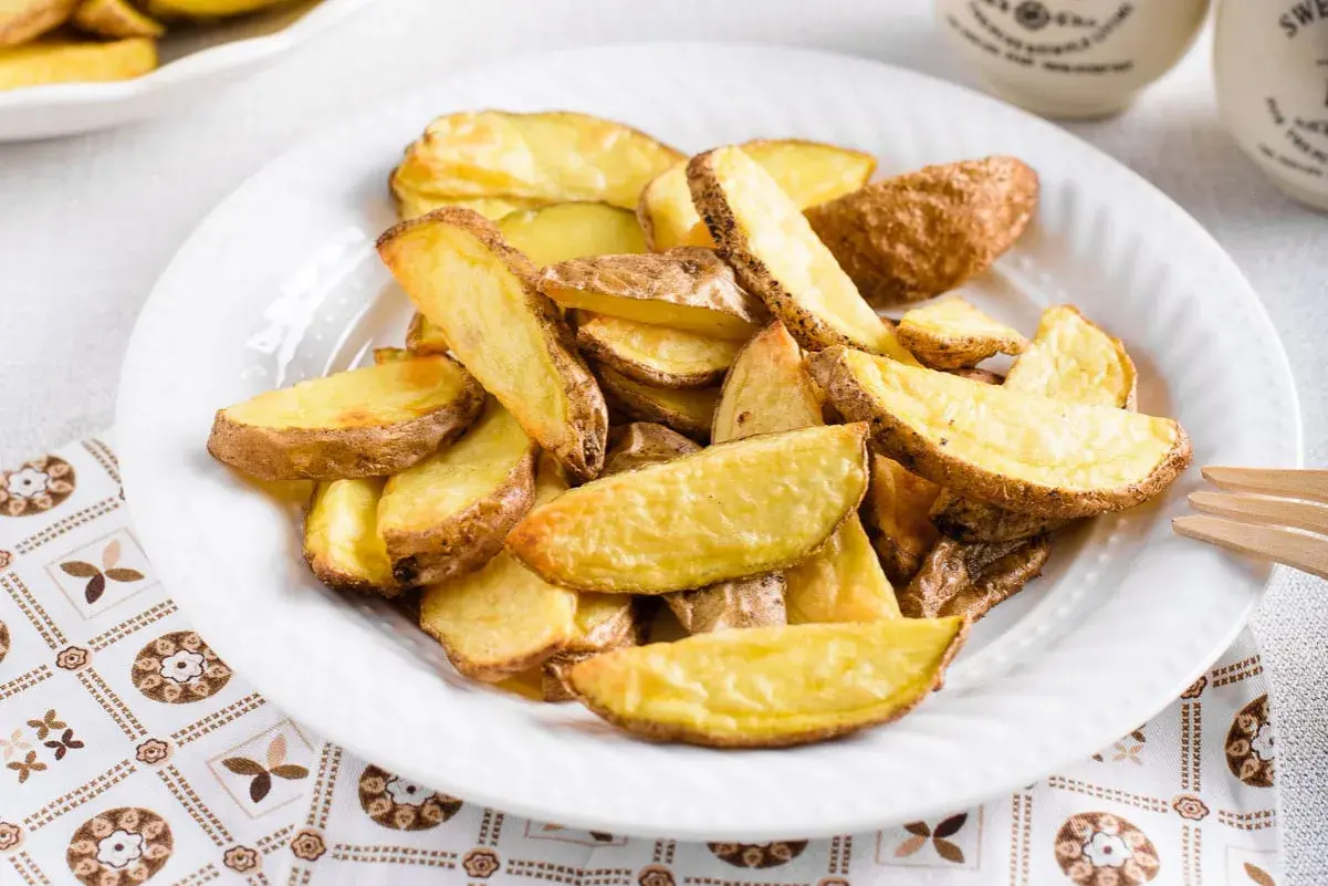 Patate a spicchi dorate e croccanti, appena sfornate dalla friggitrice ad aria, servite su un piatto bianco.