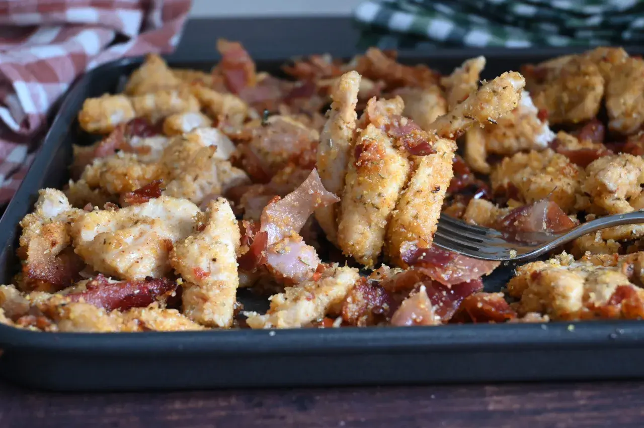 Straccetti di pollo al forno croccanti e saporiti, con fette di pancetta croccante, serviti in una teglia.