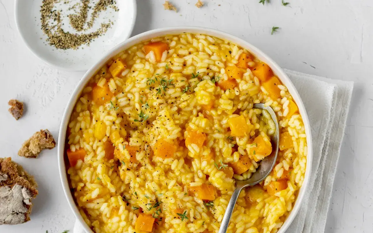 Un cremoso risotto con la zucca, guarnito con timo fresco e pepe nero macinato. Accanto, pane rustico e una ciotolina di pepe.