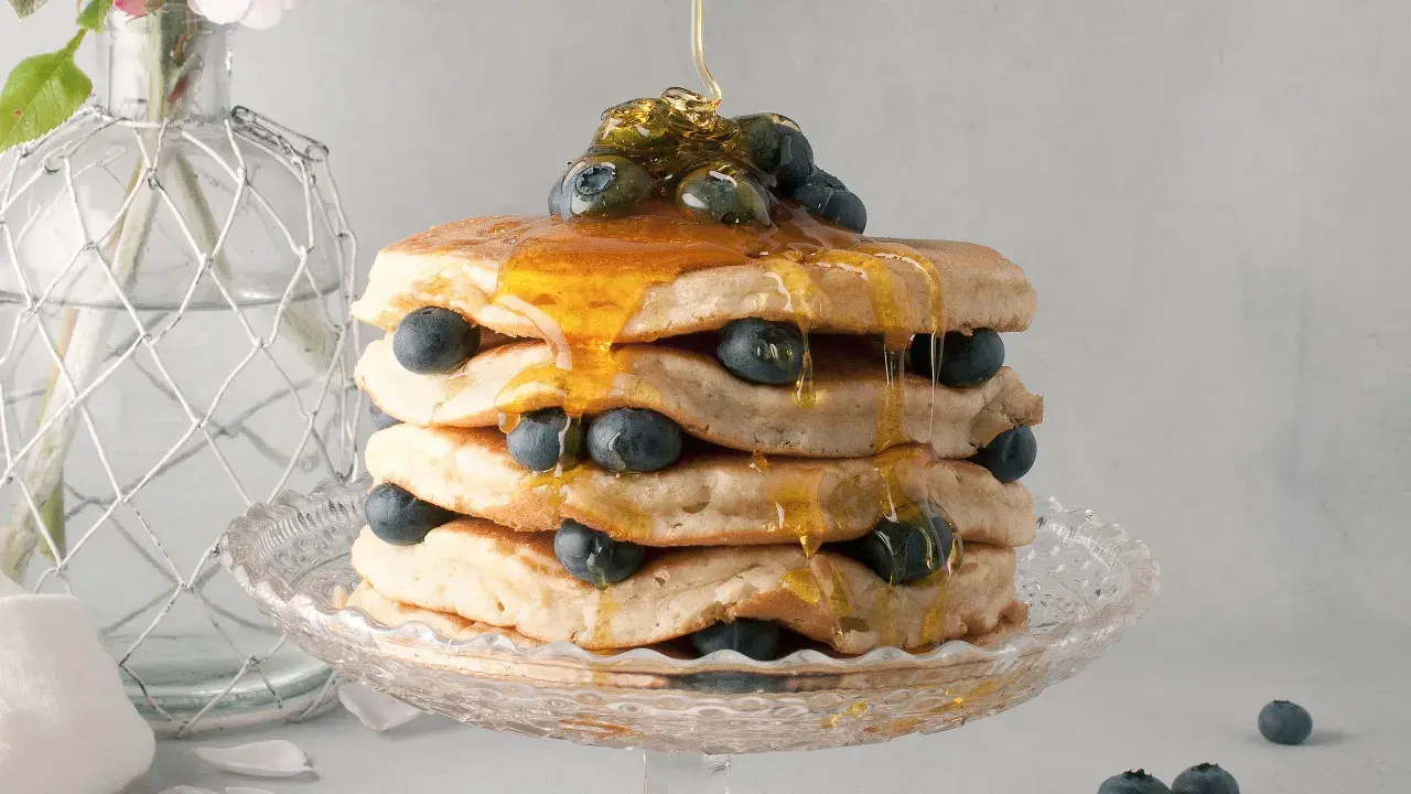 Pancake senza latte, una torre dorata con mirtilli freschi e sciroppo d'acero che cola. Delizioso e leggero, perfetto per ogni momento.