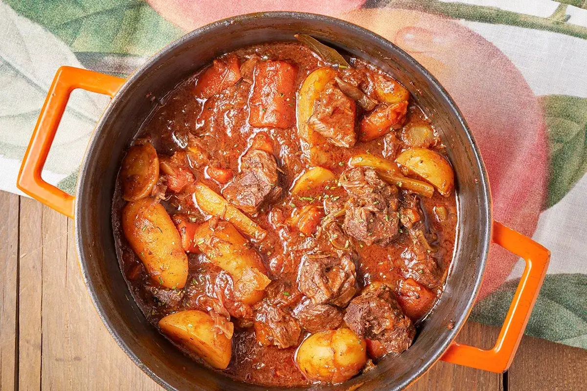 Un saporito spezzatino di vitello con patate e carote, cotto lentamente in un tegame di ghisa arancione.