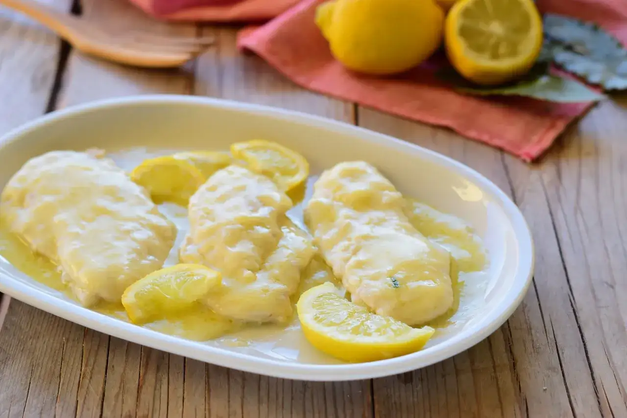 Scaloppine al limone succulente su un piatto bianco, guarnite con fette di limone fresco.