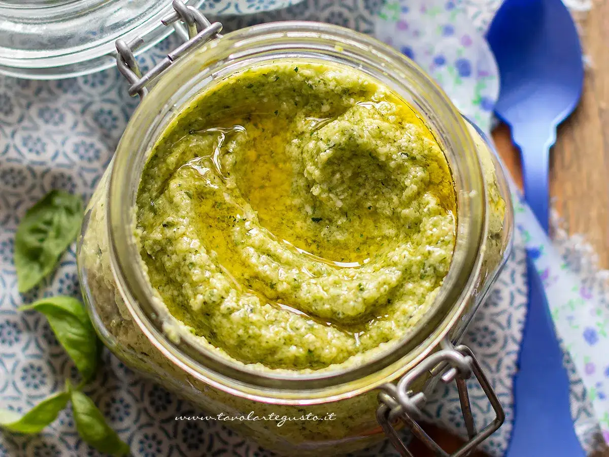 Vaso di vetro pieno di pesto di zucchine fatto in casa, con olio d'oliva che luccica in superficie.
