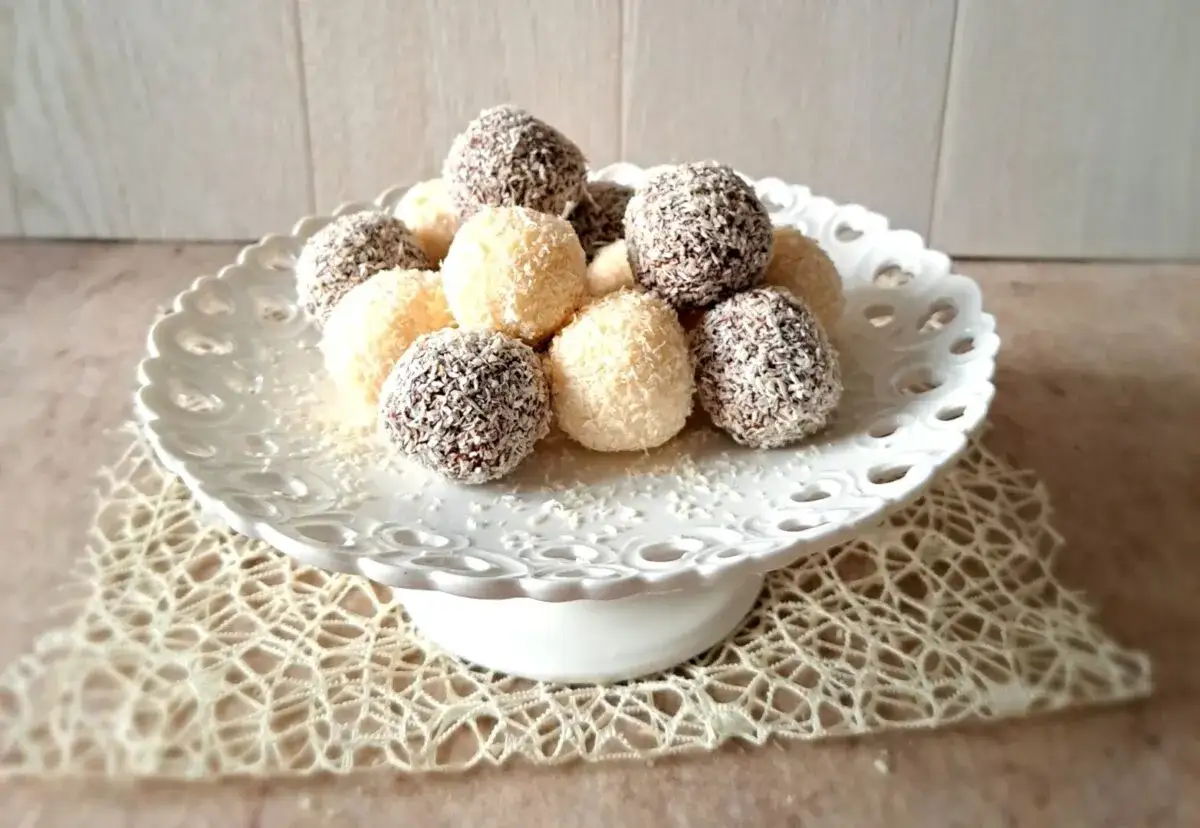 Deliziose palline di cocco, alcune al cioccolato, altre bianche, disposte su un'alzata di ceramica traforata.