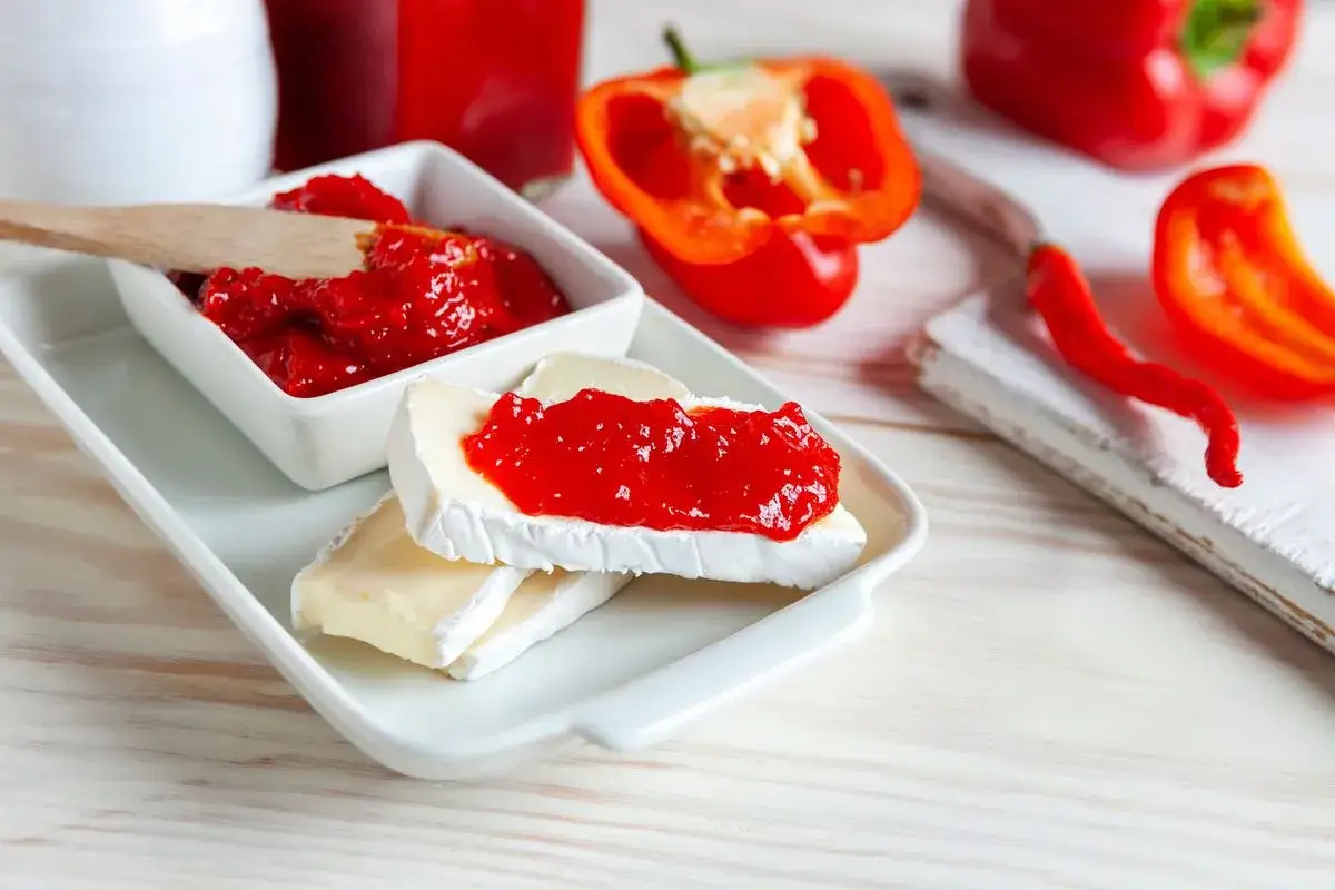 Fette di formaggio brie con marmellata di peperoni, accompagnate da peperoni rossi freschi.