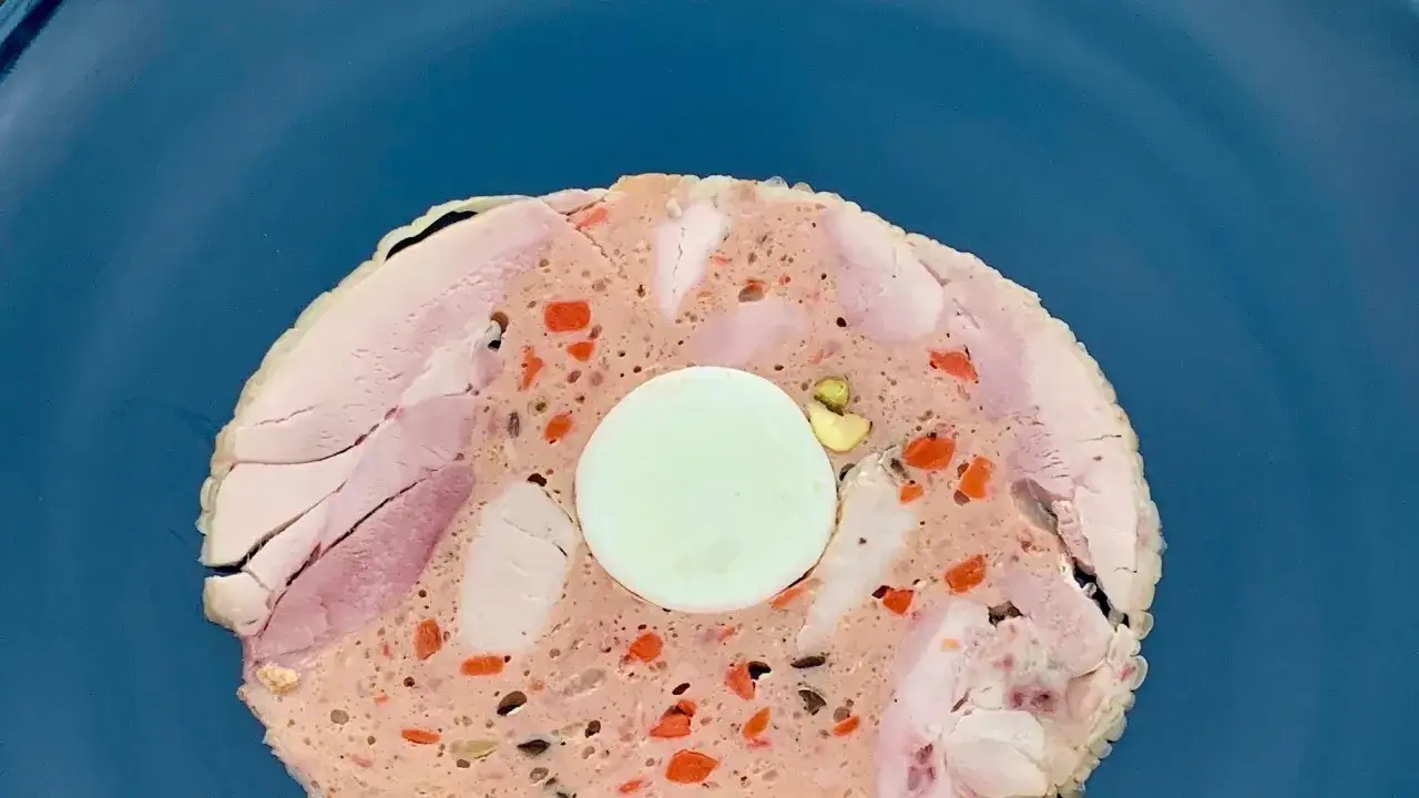 Fetta di galantina di pollo con uovo sodo al centro, carote e pistacchi.