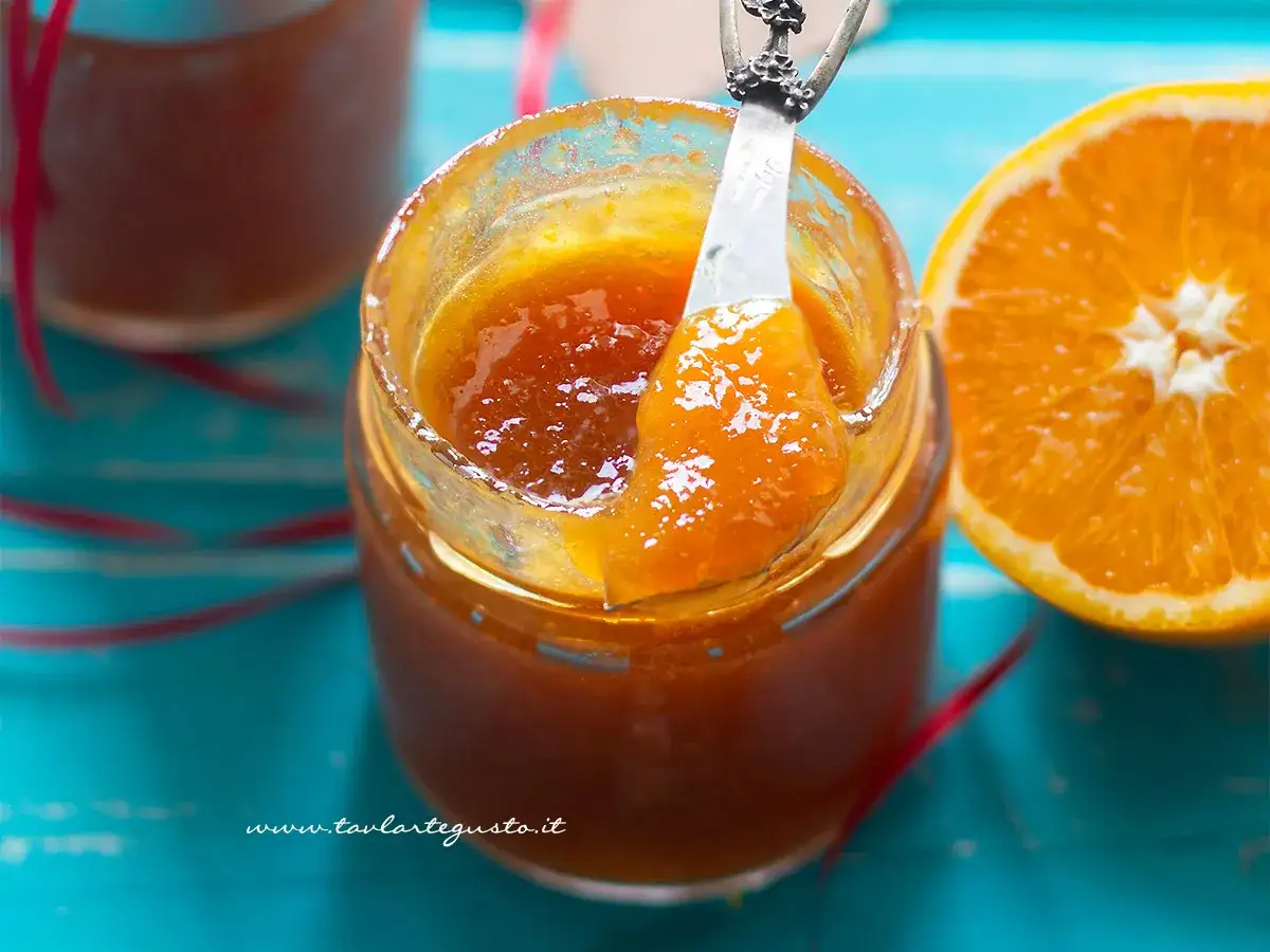 Un vasetto di marmellata di arance fatto in casa, con una fetta d'arancia accanto. La marmellata è lucida e invitante.