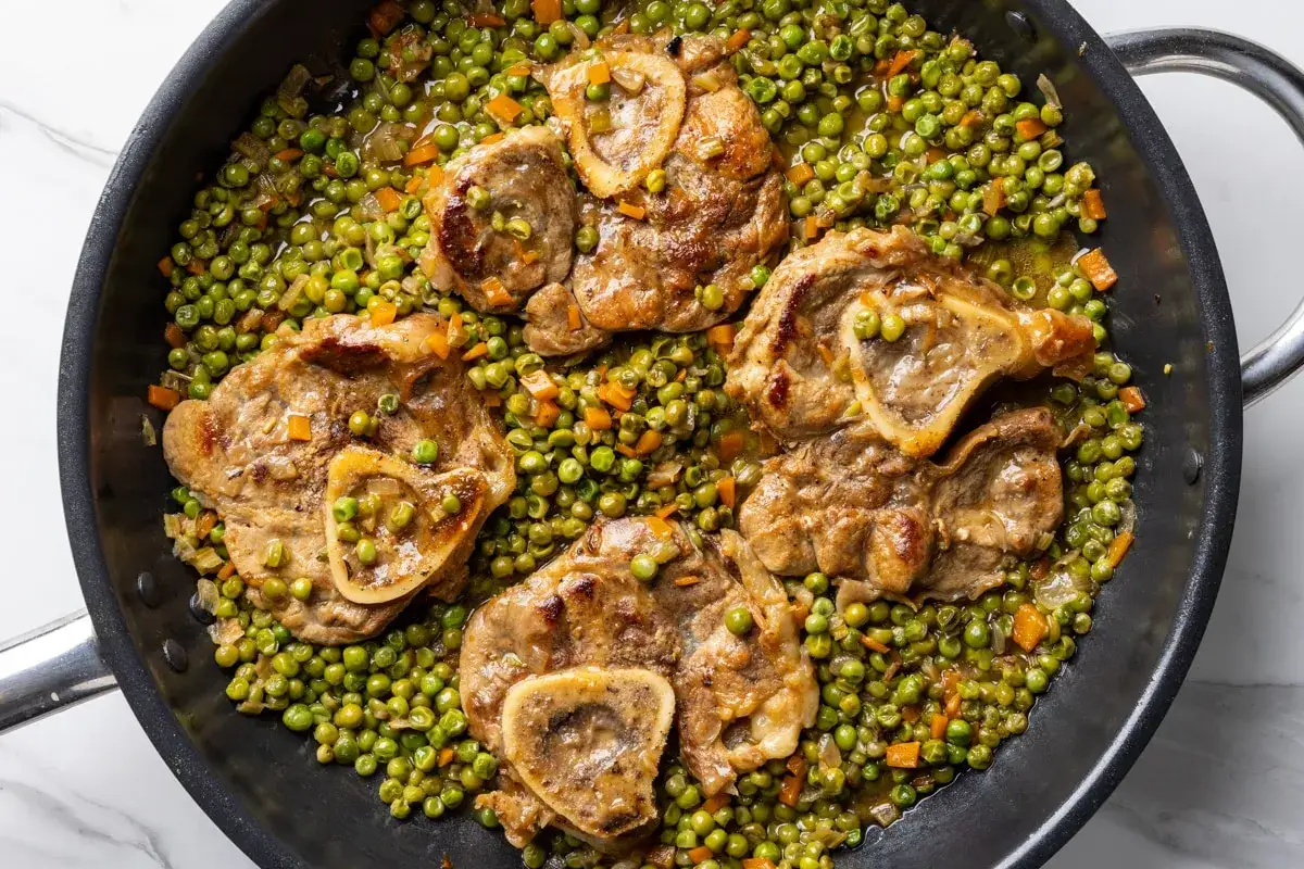 Ossobuco con piselli in padella, un piatto succulento con carne tenera e piselli freschi, pronto per essere gustato.