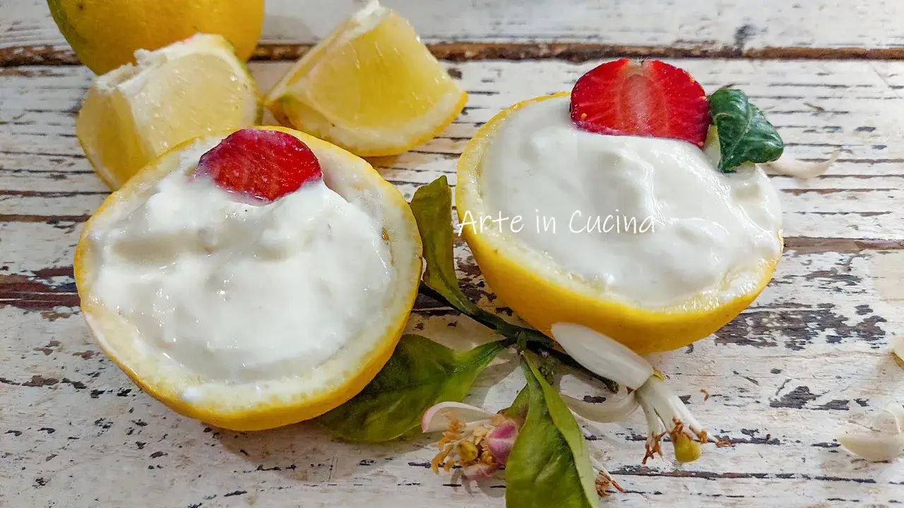 Deliziosa mousse al limone servita in scorze di limone, guarnita con fragola e foglioline verdi.