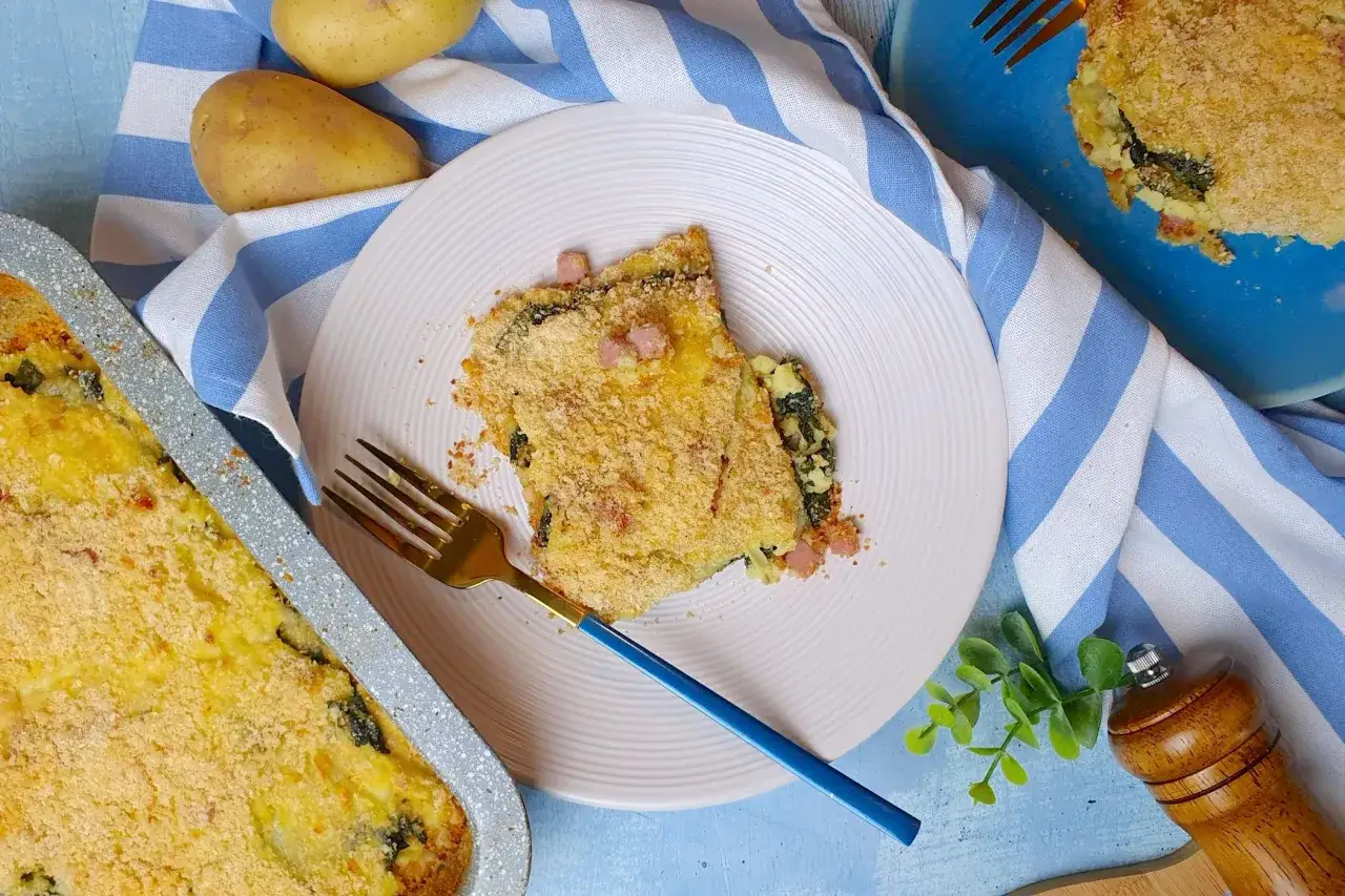 Una fetta di parmigiana di patate, con spinaci e pancetta, dorata e croccante, servita su un piatto bianco.