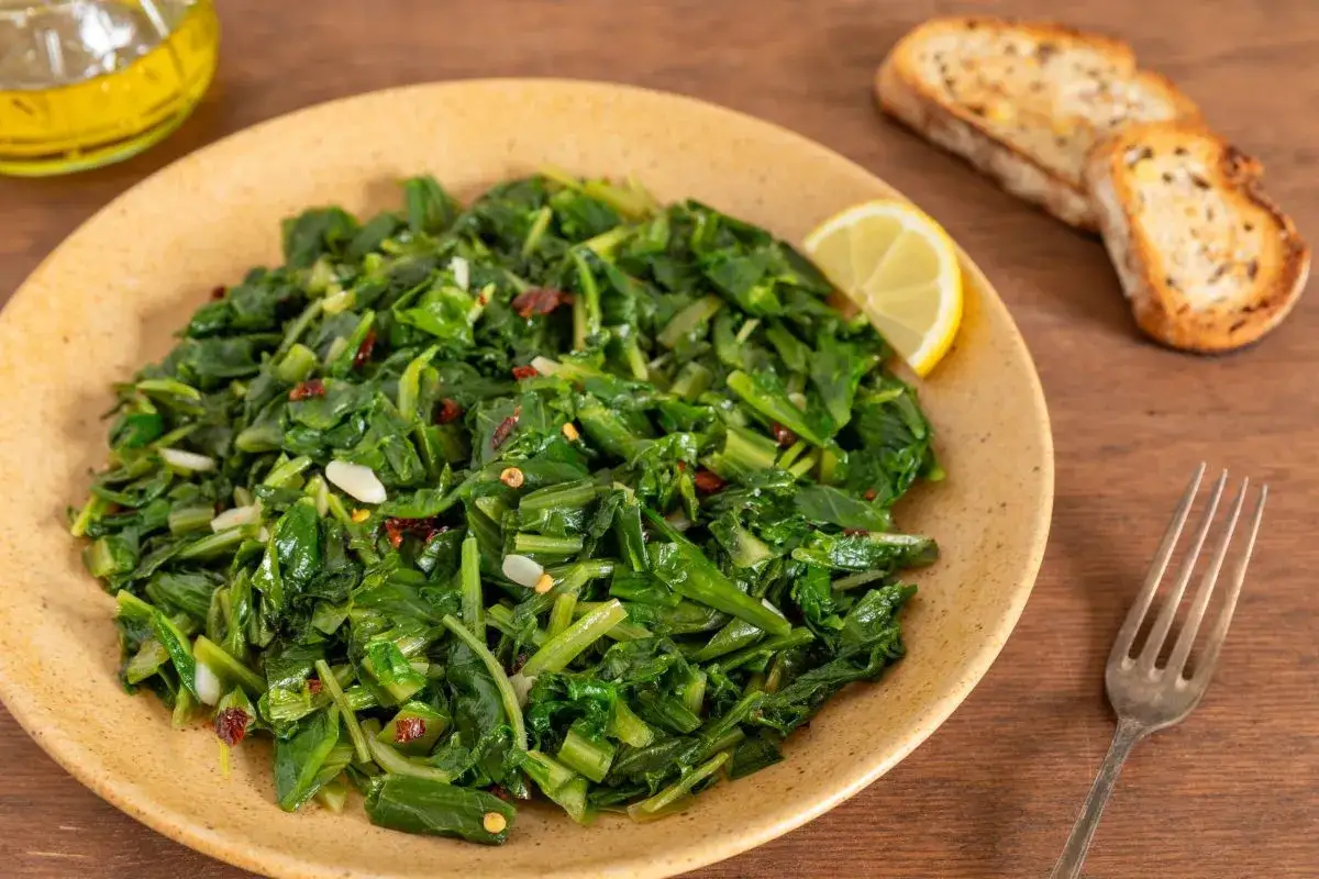Cicoria in padella, un contorno saporito con aglio e peperoncino, servita con pane tostato e spicchio di limone.