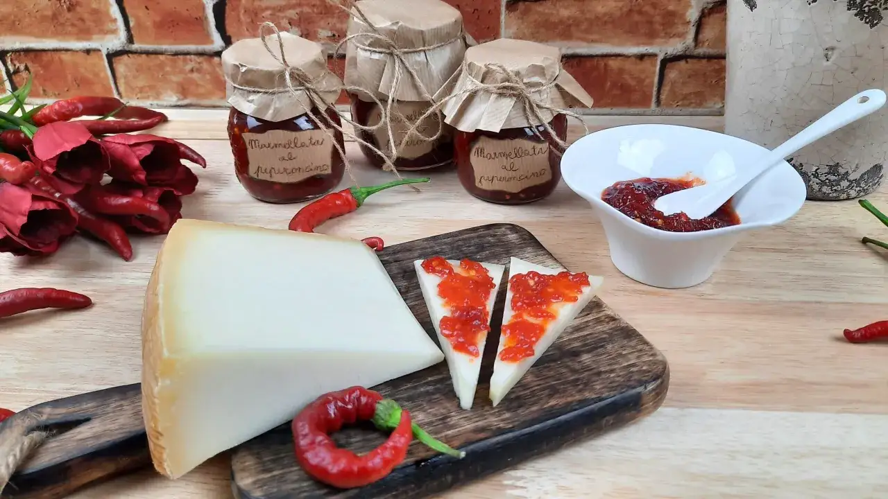 Tre vasetti di marmellata di peperoncino, formaggio e peperoncini rossi su un tagliere di legno.