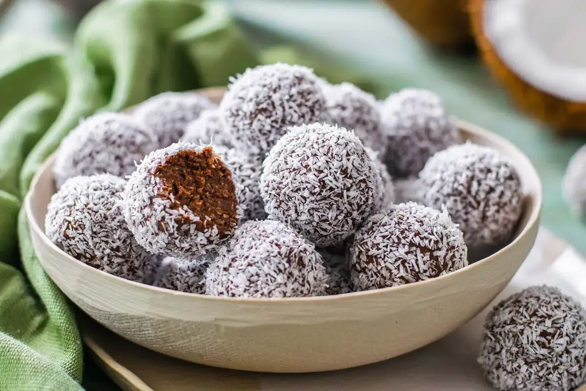 Una ciotola piena di dolcetti al cocco, uno è morso mostrando il ripieno al cioccolato.