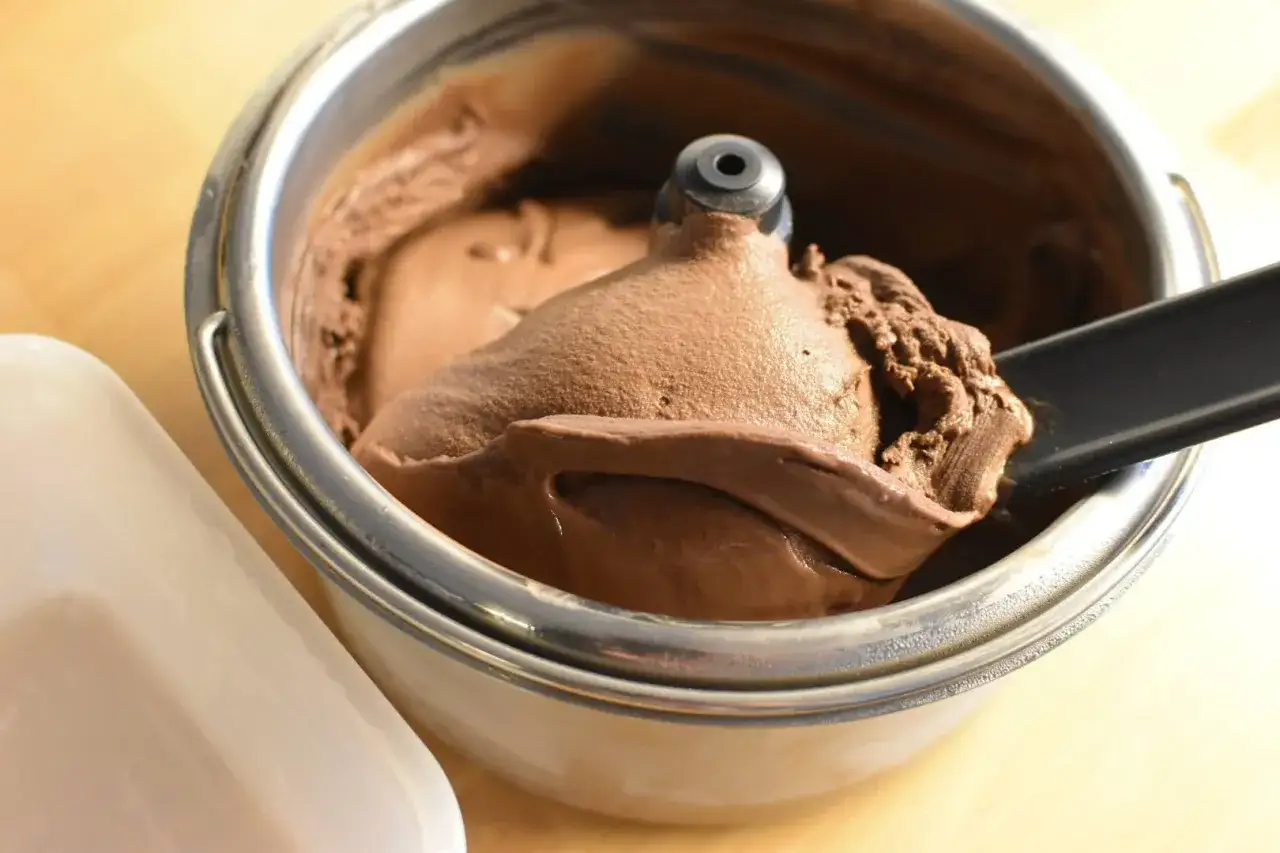 Un cucchiaio nero preleva una generosa porzione di cremoso gelato fatto in casa al cioccolato da una gelatiera.