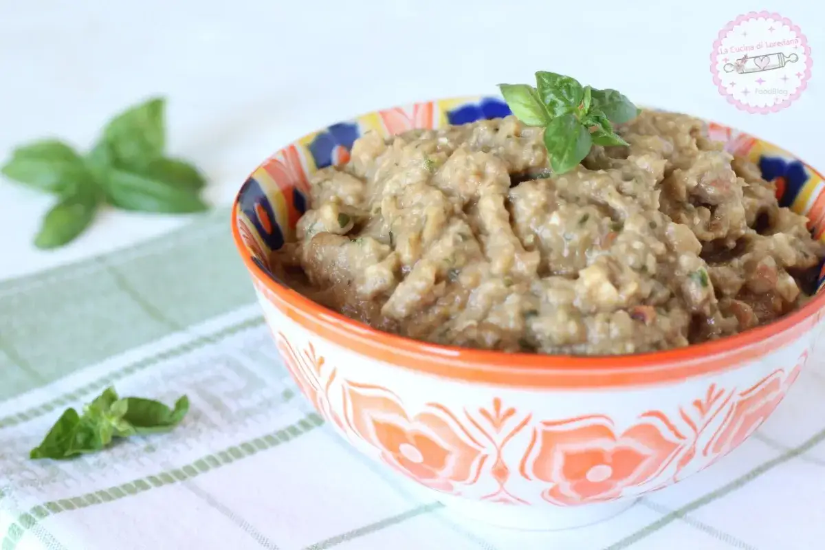 Una ciotola colorata piena di pesto di melanzane, guarnita con basilico fresco. Perfetto per un antipasto estivo.
