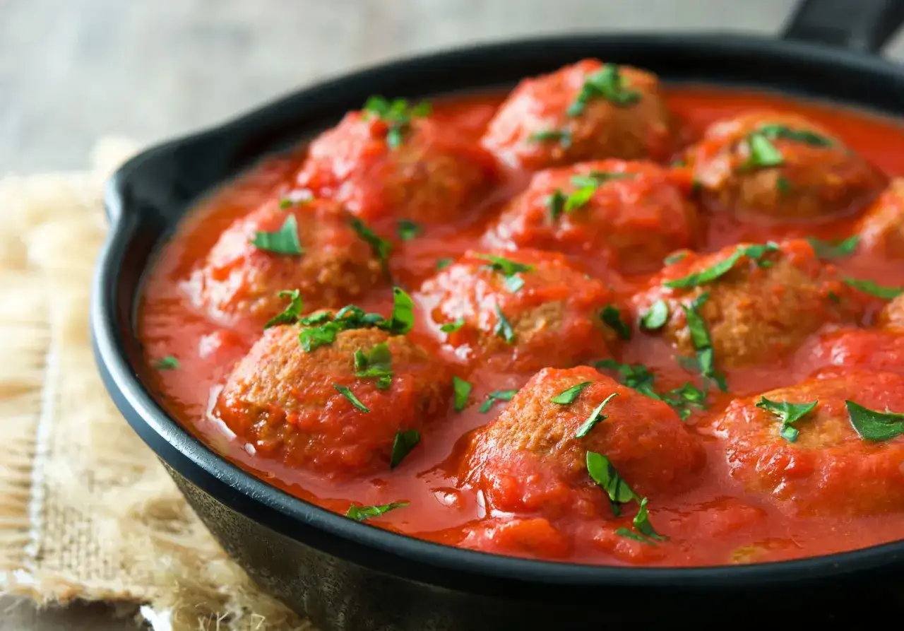 Polpette di carne morbide in salsa di pomodoro, guarnite con prezzemolo fresco, servite in una padella di ghisa.