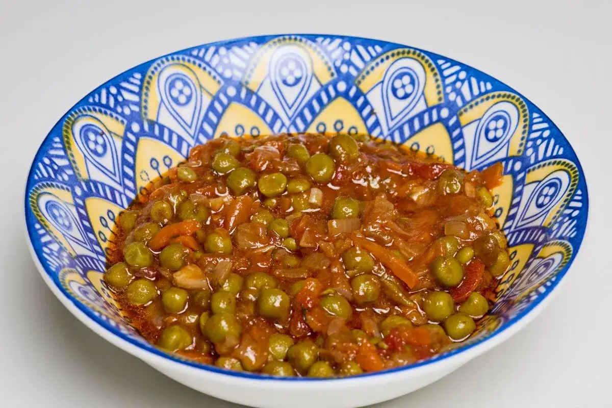Un piatto invitante di piselli in umido, con carote e cipolla, servito in una ciotola decorata con motivi blu e gialli.