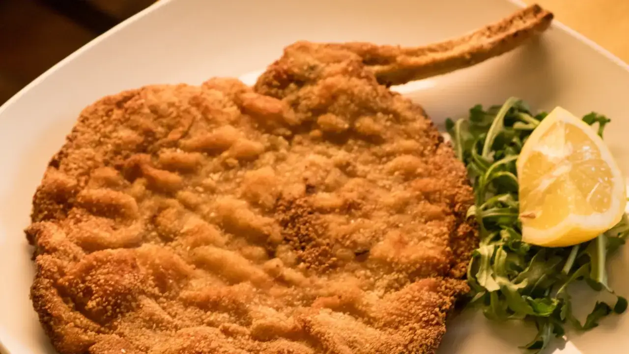 Una croccante cotoletta alla milanese dorata, servita con rucola fresca e una fetta di limone.