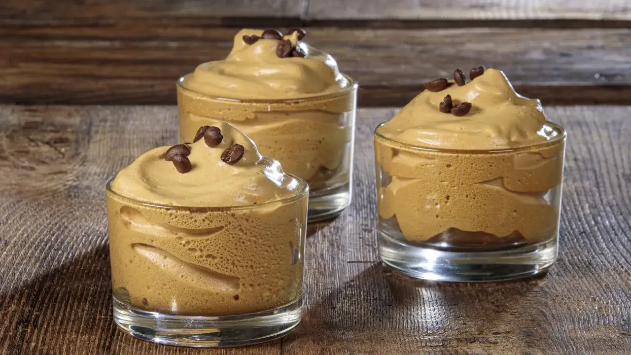 Tre bicchierini di deliziosa crema caffè fredda, guarniti con chicchi di caffè, su un tavolo di legno rustico.