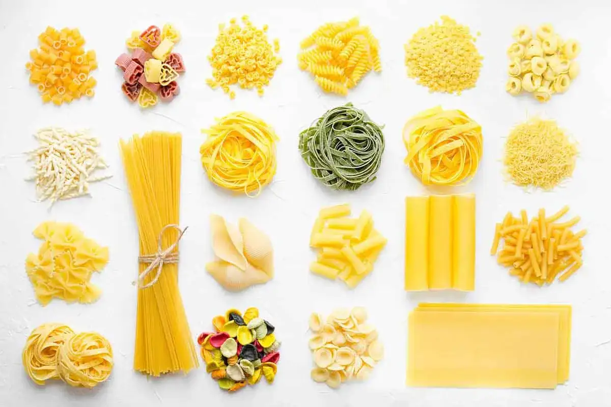 Una variet&agrave; di pasta fatta in casa, da spaghetti a farfalle, con forme e colori diversi, pronta per essere cucinata.
