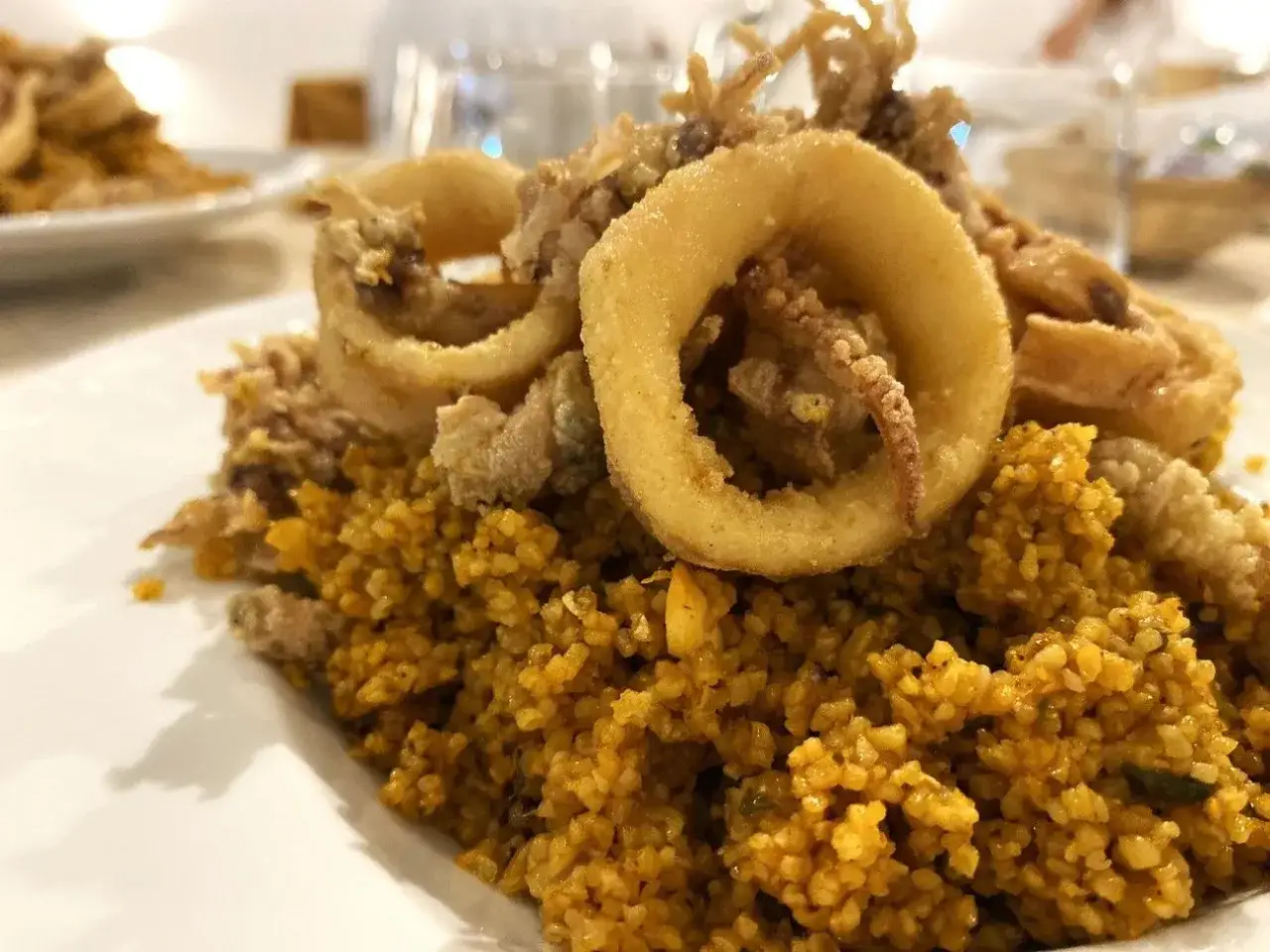 Un invitante cous cous di pesce con anelli di calamari fritti croccanti e tentacoli che spuntano. Un piatto saporito e colorato.