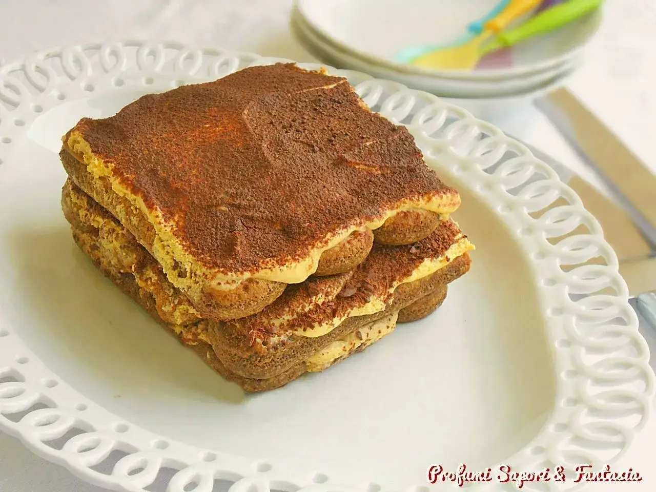 Un goloso tiramisù giallo zafferano, stratificato con savoiardi e crema, spolverato di cacao.