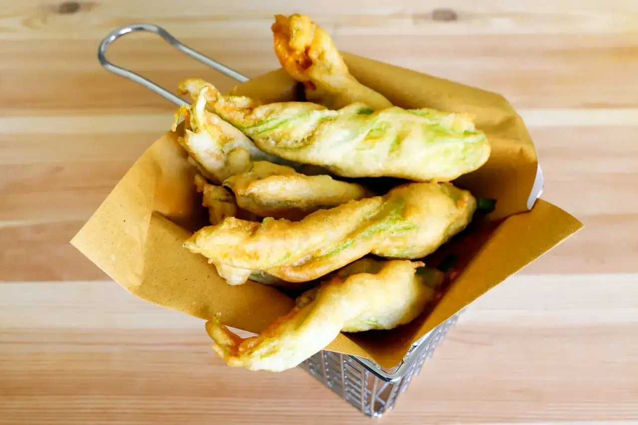 Fiori di zucca fritti, dorati e croccanti, serviti in un cestino di metallo foderato con carta marrone.