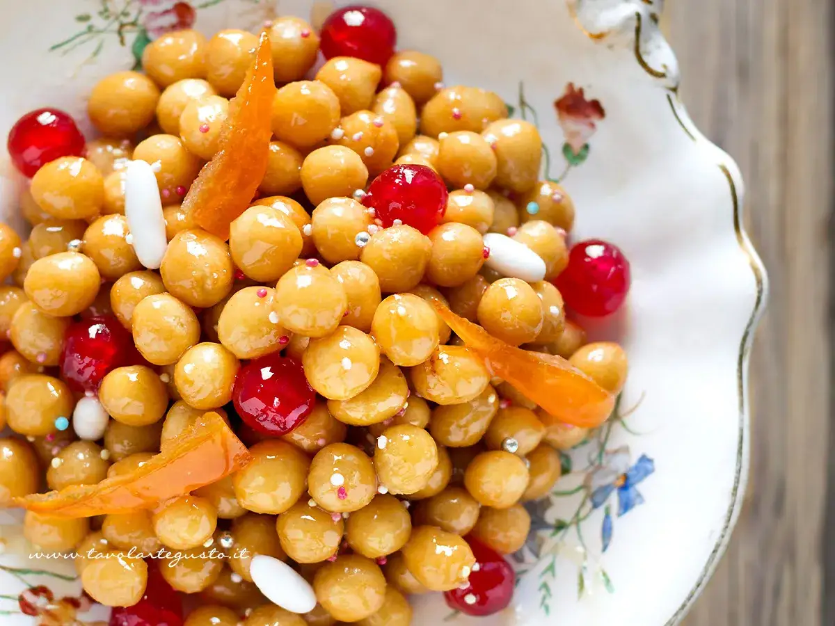Struffoli ricetta della nonna: palline dorate glassate, ciliegie rosse e scorzette d'arancia in un piatto decorato.