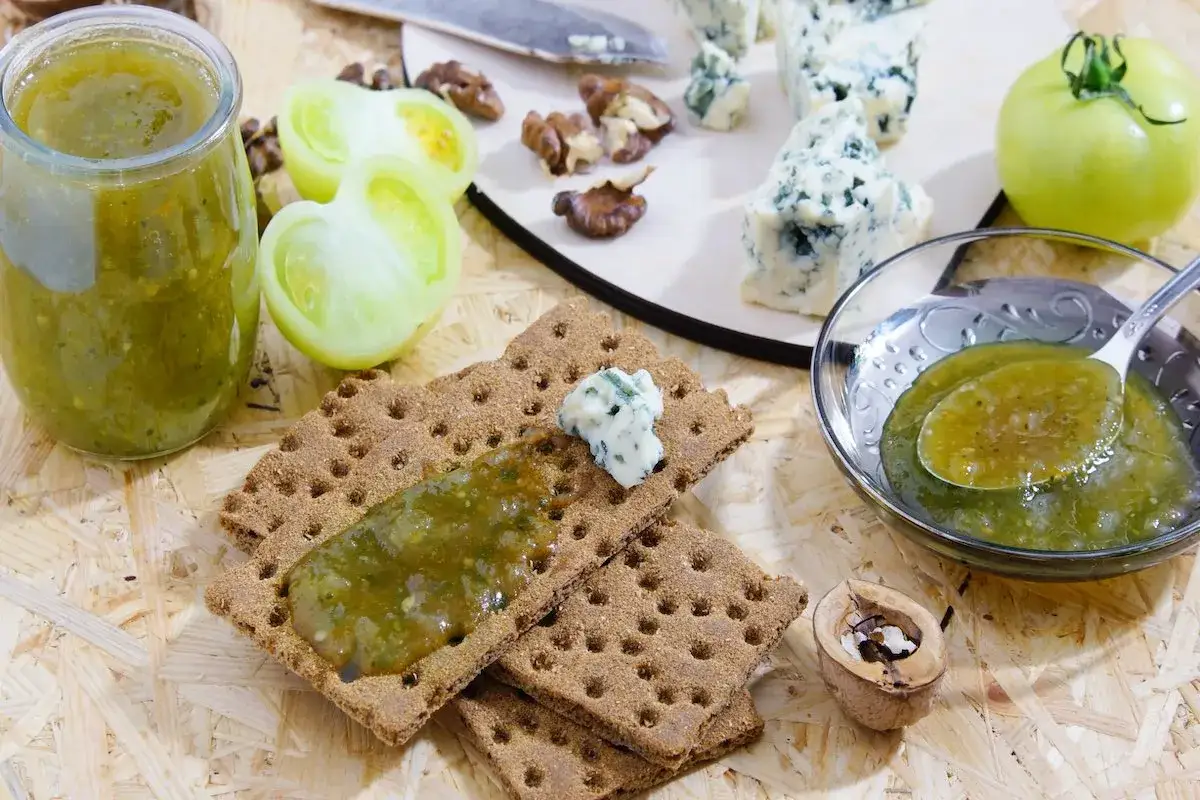 Un vasetto e una ciotola di marmellata di pomodori verdi, serviti con cracker, formaggio blu e noci.