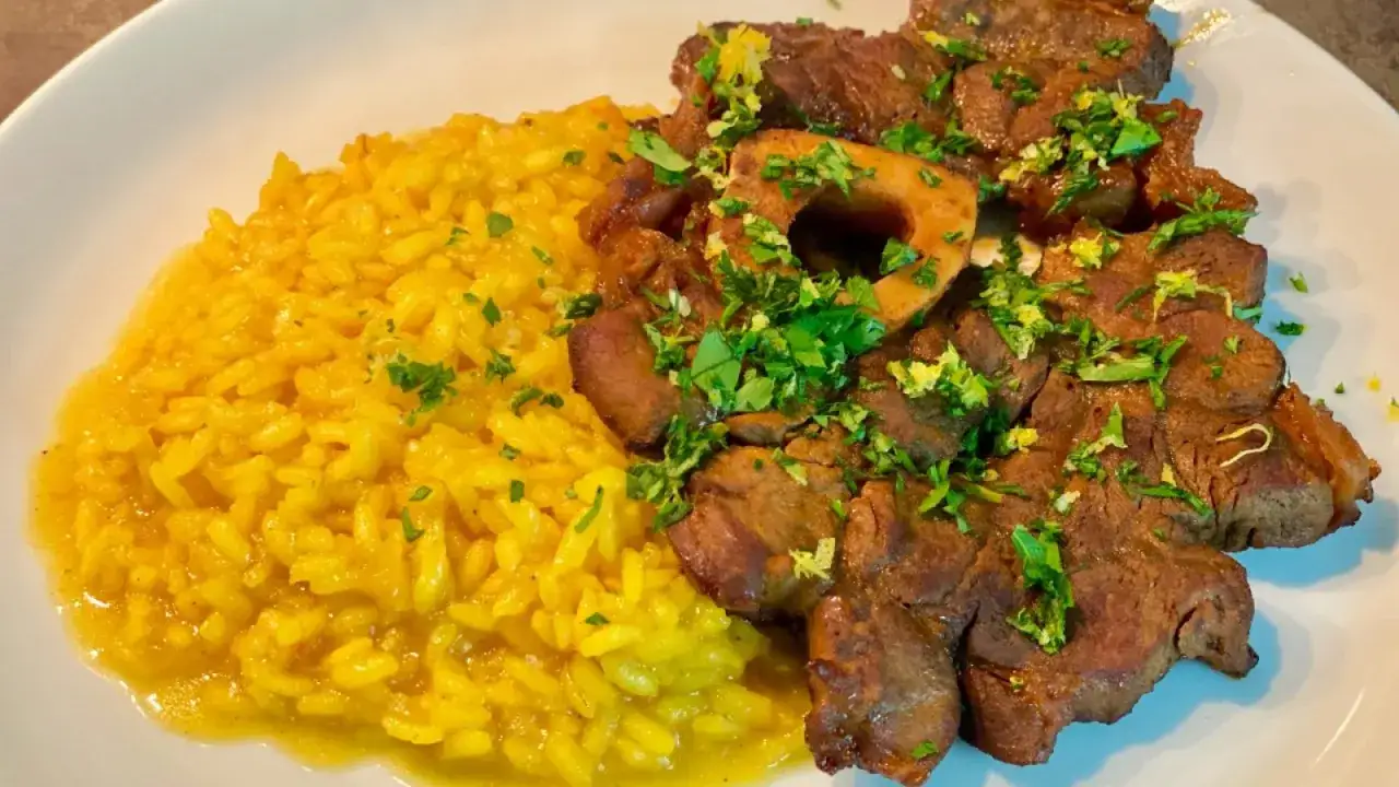 Ossobuco alla milanese con risotto giallo, guarnito con prezzemolo tritato e scorza di limone.