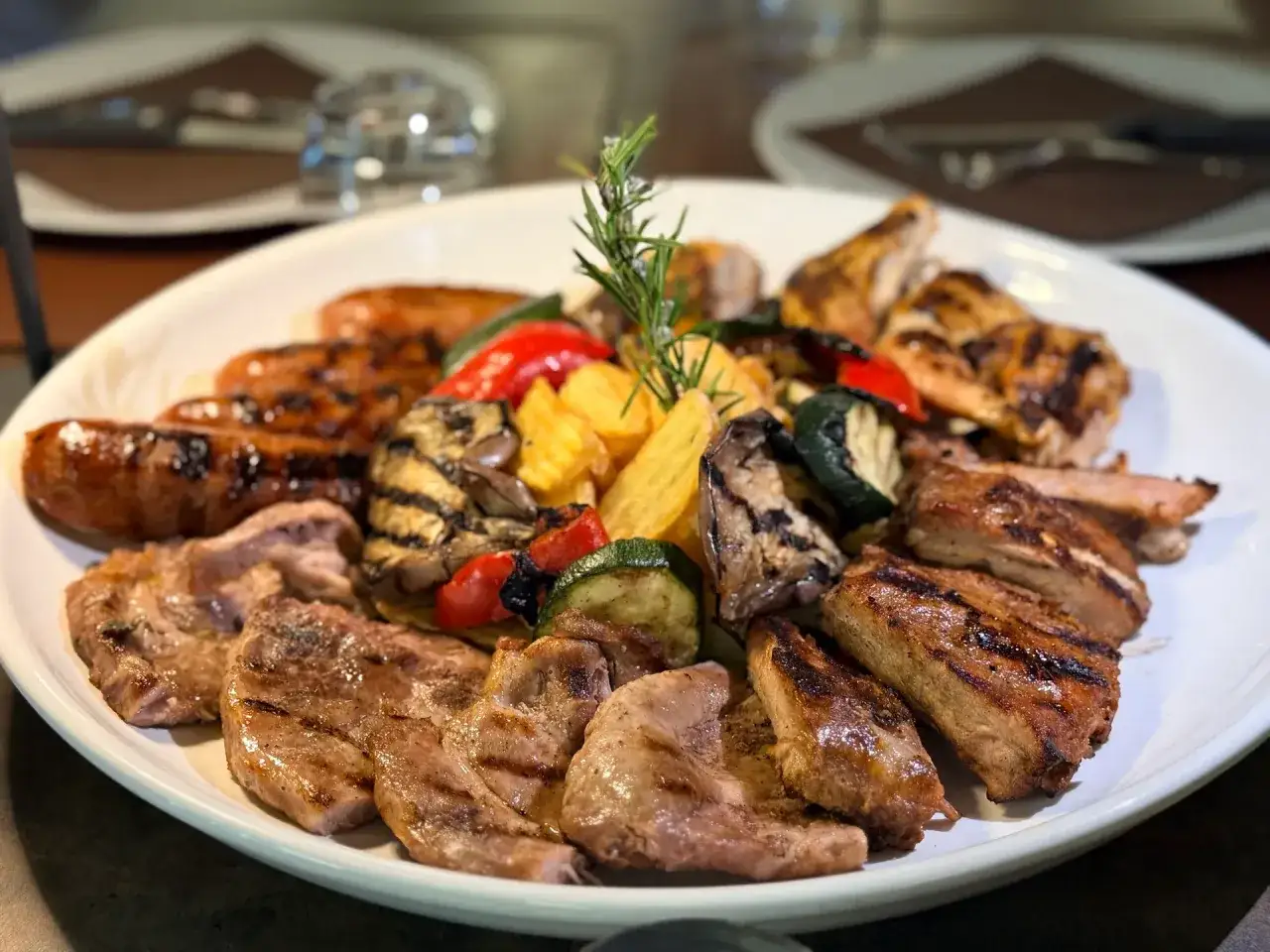 Un piatto invitante di grigliata di carne, con salsicce, costolette, pollo e verdure grigliate, guarnito con rosmarino.