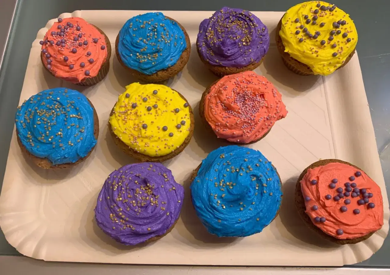 Dieci cupcake colorati con crema al burro, decorati con zuccherini dorati e perline.