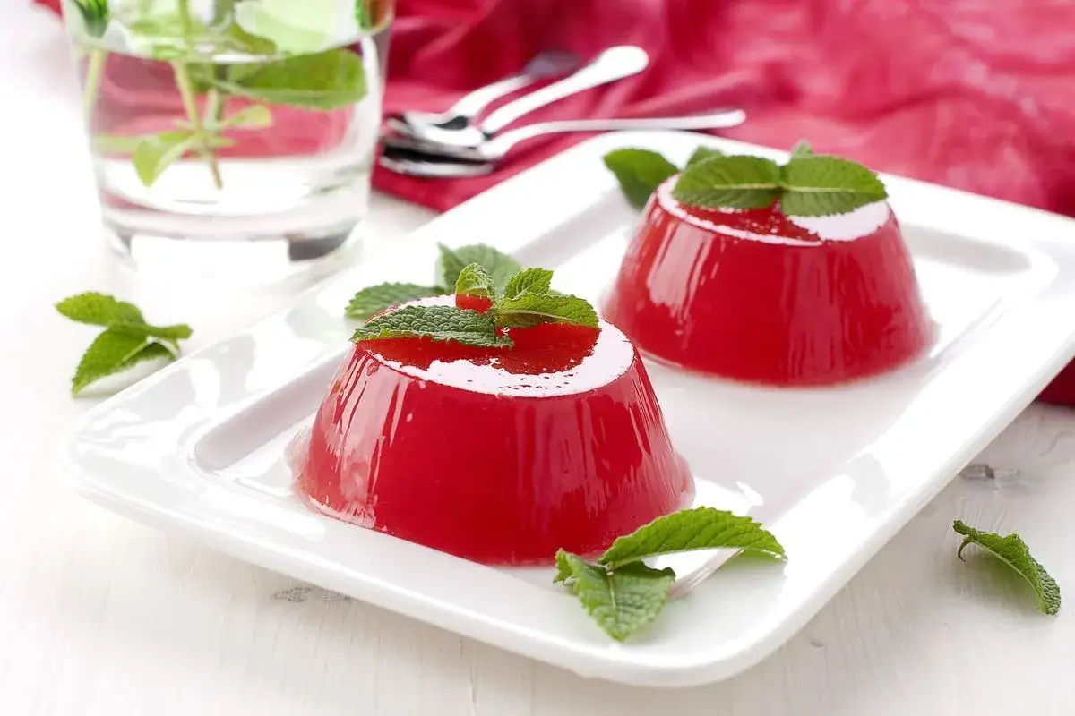 Due gelatine rosse, un delizioso gelo di anguria, guarnite con menta fresca, su un piatto bianco.