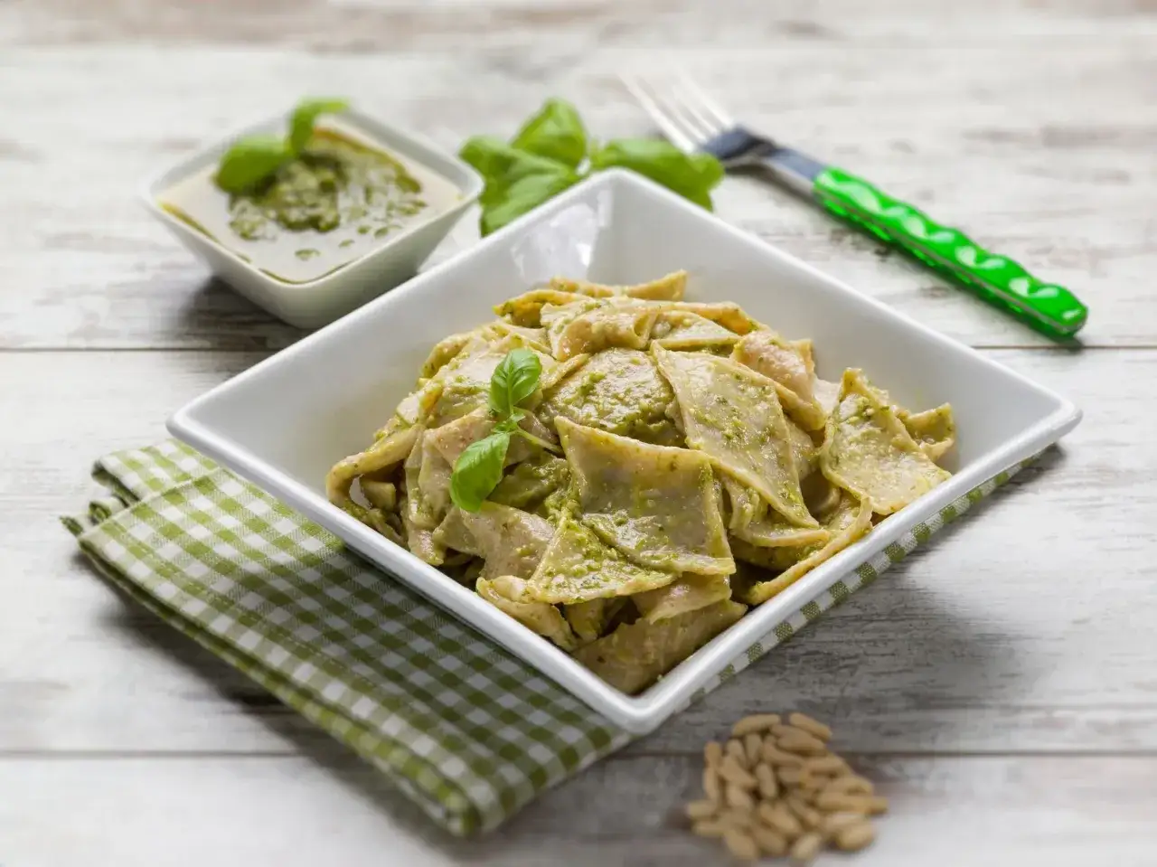 Testaroli al pesto, un piatto di pasta fresca condita con salsa verde profumata, guarnito con basilico e pinoli.