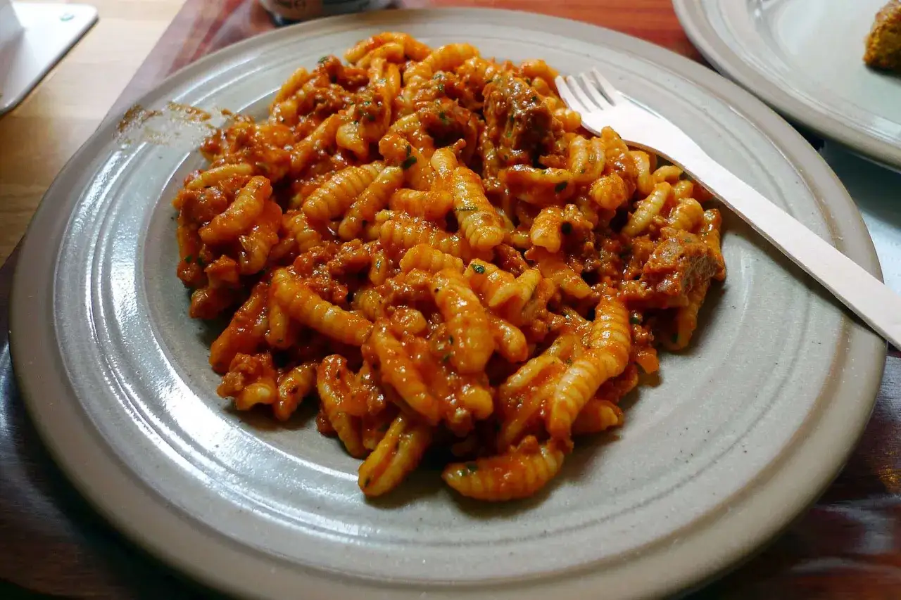 Un piatto di malloreddus alla campidanese, pasta sarda con sugo di salsiccia e pomodoro, pronto per essere gustato.