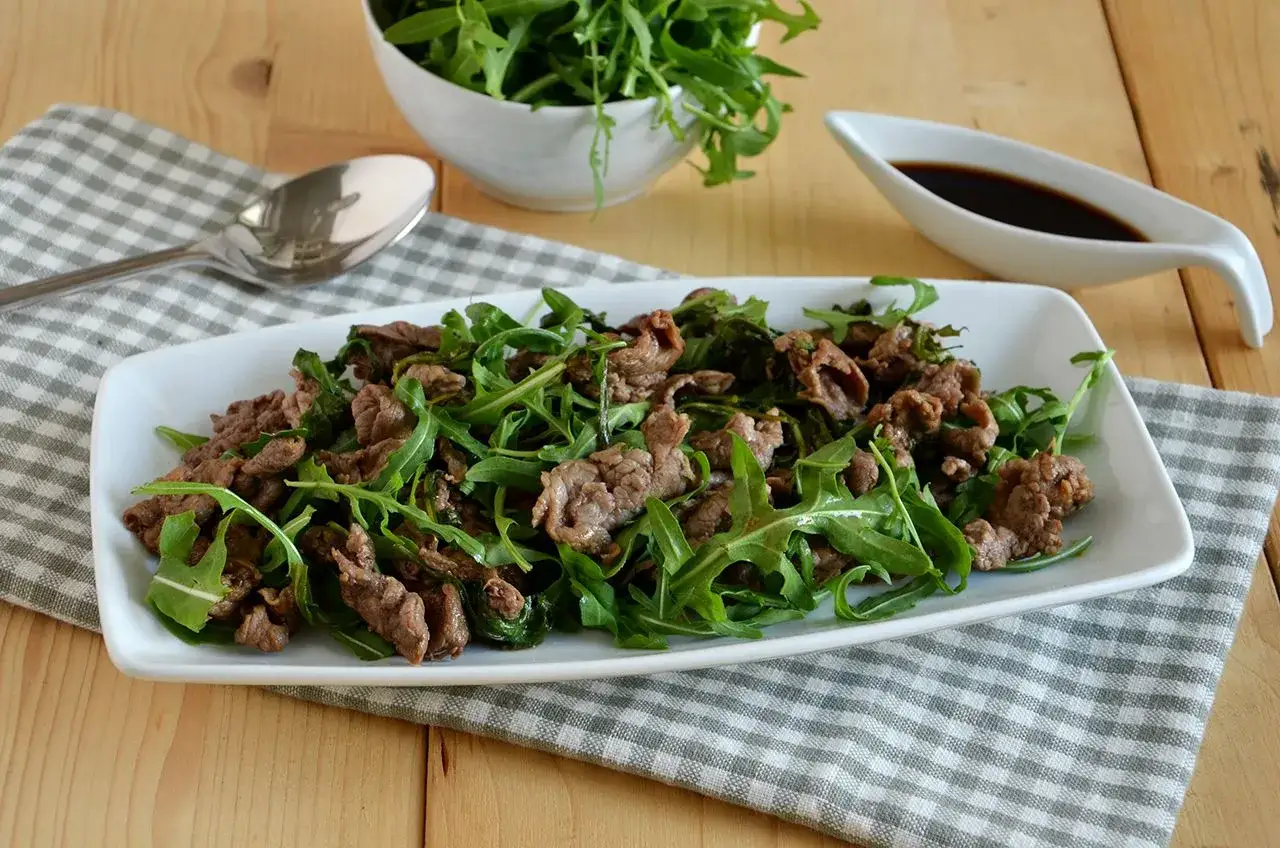 Deliziosi straccetti di vitello saltati con rucola fresca, serviti su un piatto bianco.