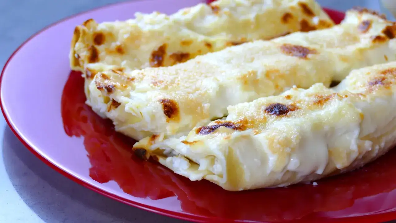 Tre invitanti cannelloni di carne, dorati al forno e ricoperti di besciamella cremosa, serviti su un piatto rosso brillante.