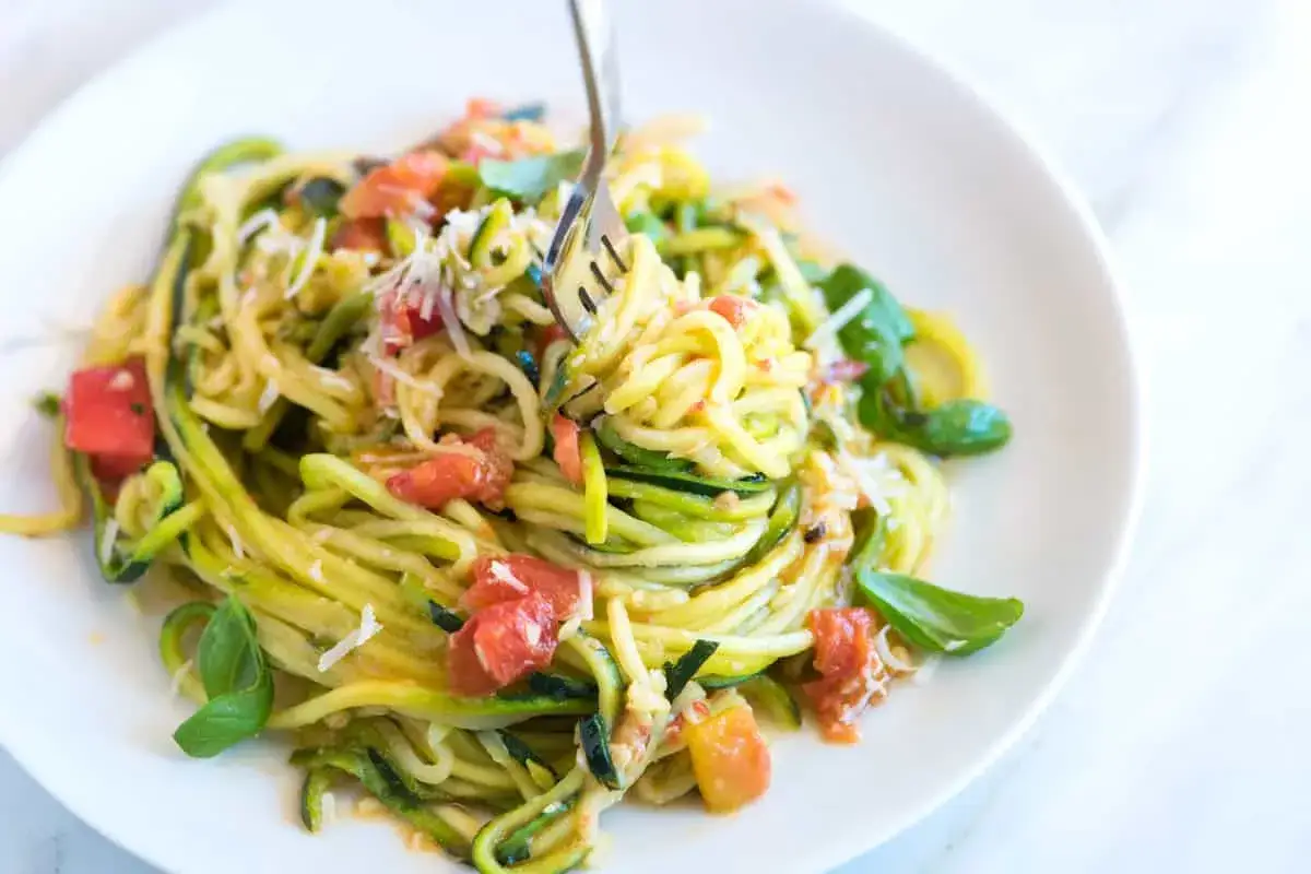 Un piatto di spaghetti di zucchine freschi, conditi con pomodoro e basilico, pronti per essere gustati con una forchettata.