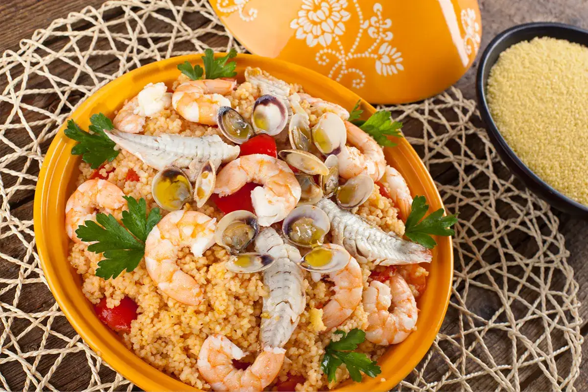 Piatto di cous cous con gamberi, vongole e pesce, un'ottima ricetta cous cous originale, guarnito con prezzemolo.