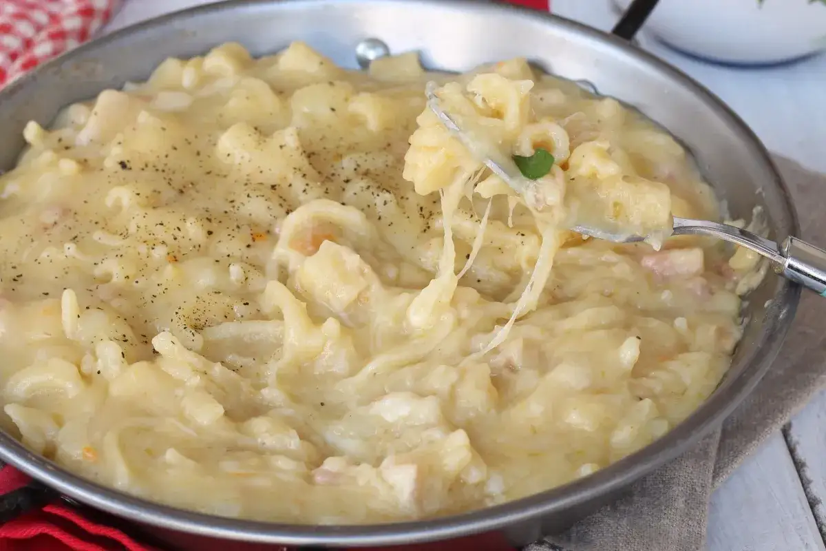 Una padella piena di cremosa pasta e patate, con formaggio filante e una spolverata di pepe nero.