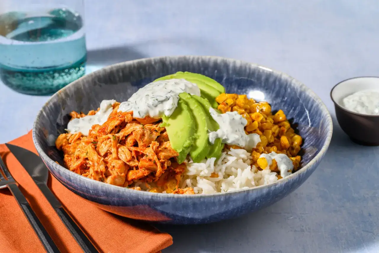 Un invitante piatto di riso con pollo sfilacciato, mais, avocado e una salsa cremosa.