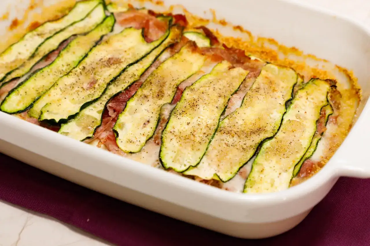 Parmigiana di zucchine appena sfornata, con fette sottili di zucchine grigliate, prosciutto e formaggio filante, cosparsa di pepe nero.